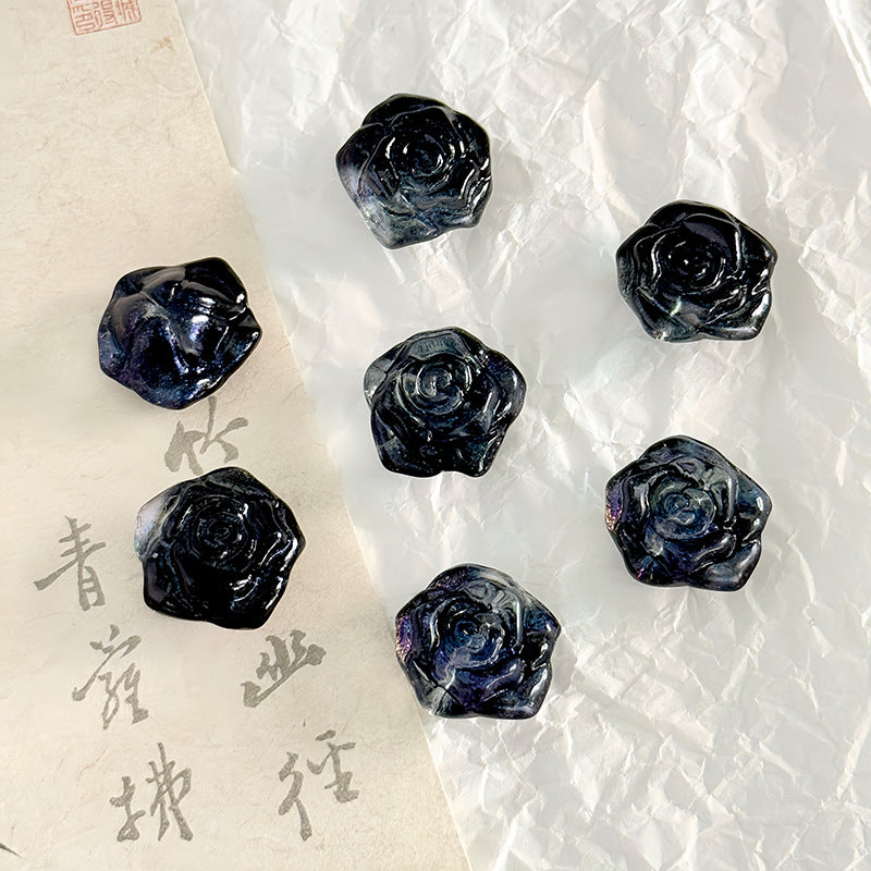 Five dark blue-gray rose-shaped cabochon beads on a split background of white paper and beige calligraphy paper