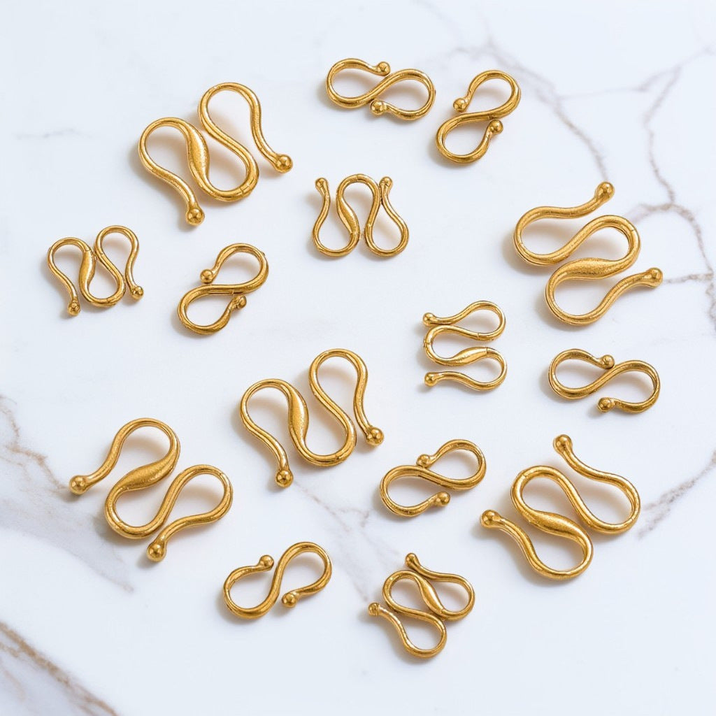 Multiple small gold-colored metal S-shaped hooks or clips scattered on a white marble surface.