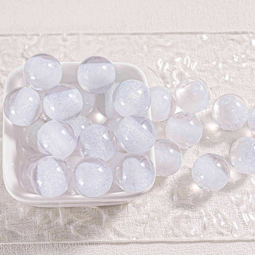 Clear round glitter beads in a white dish and scattered on textured white fabric