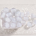 Clear round glitter beads in a white dish and scattered on textured white fabric