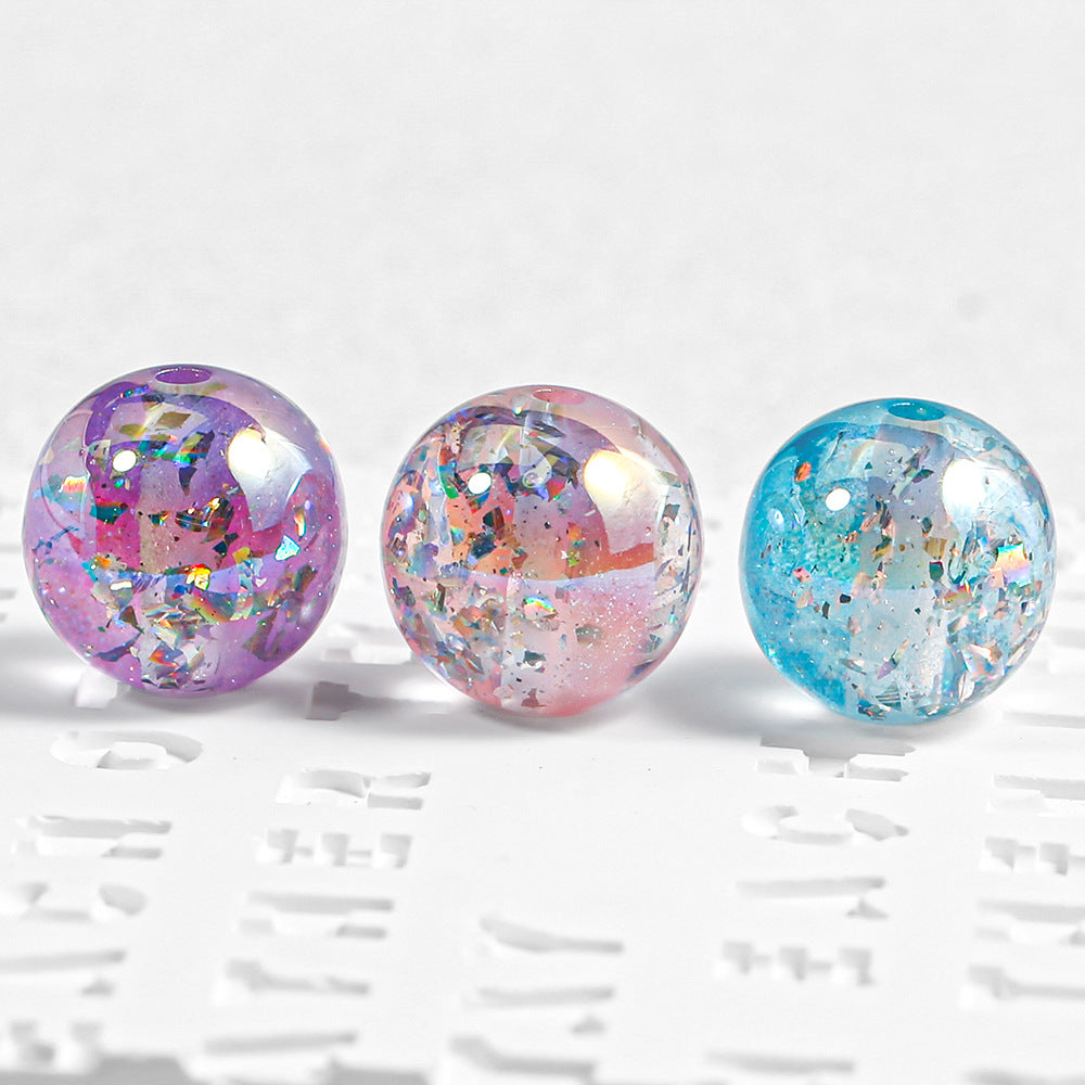 Three round resin beads with embedded glitter, shown in purple, pink, and blue colors on a white textured background.