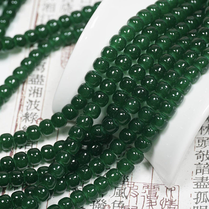 Dark green translucent round bead strands over a white ceramic stand on printed paper with Chinese characters