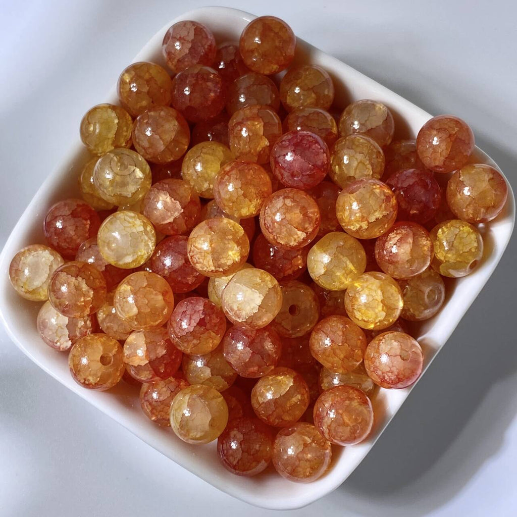Orange and amber 10mm water-dyed jade-style crackle glass beads in a white dish