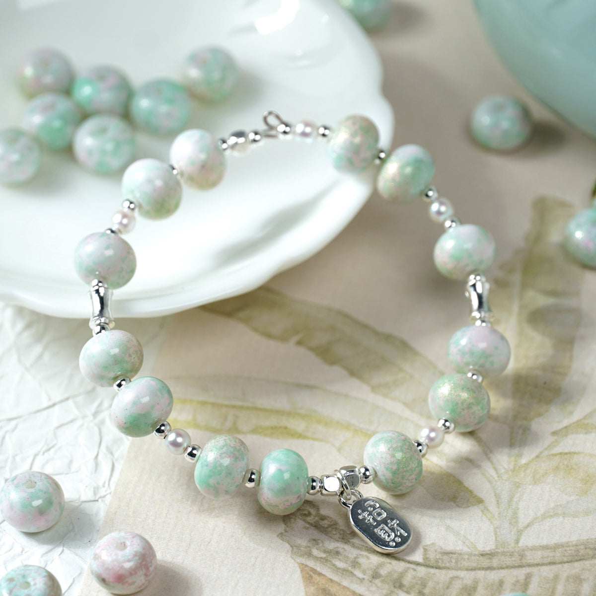Beaded bracelet with marbled mint green, white and pink round beads, silver spacers, and a small silver tag charm