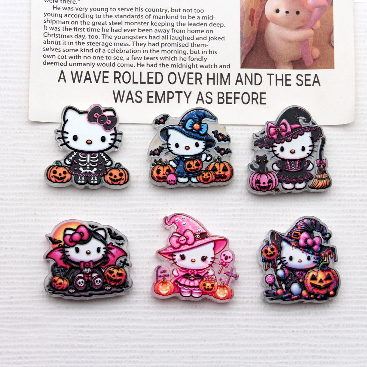 Six Hello Kitty Halloween acrylic charms with pumpkins, bats, and costumes on white surface below printed card
