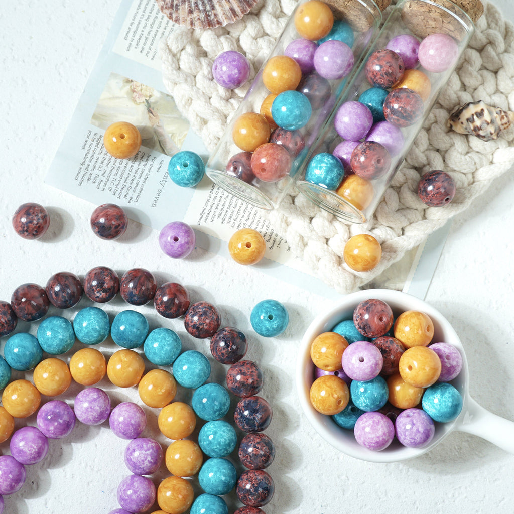 Colorful round marbled glass beads in strands, glass jars, and a white cup on a knit blanket