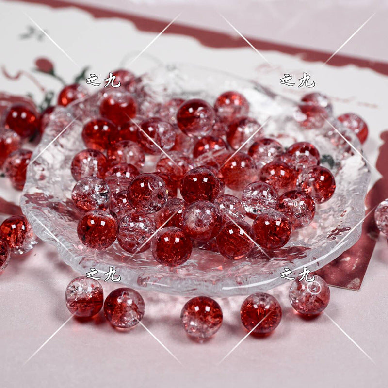 Red clear glass round beads with a crackle pattern, displayed on a clear glass dish with a few scattered around it.