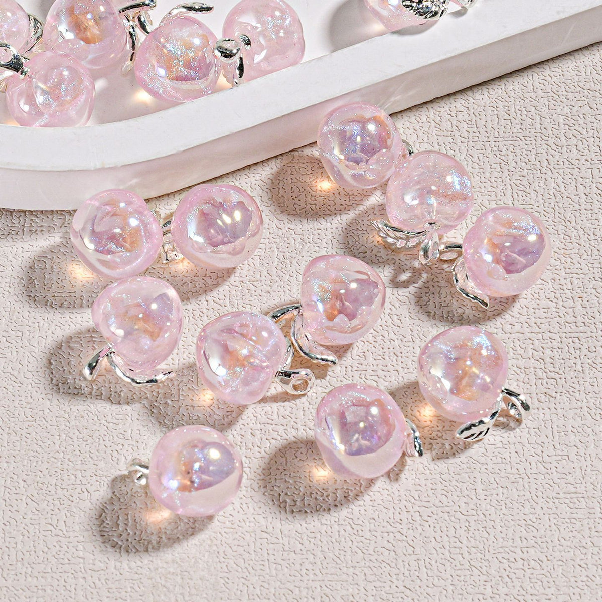 Pink translucent mini peach beads with small silver leaf accents on a textured beige surface