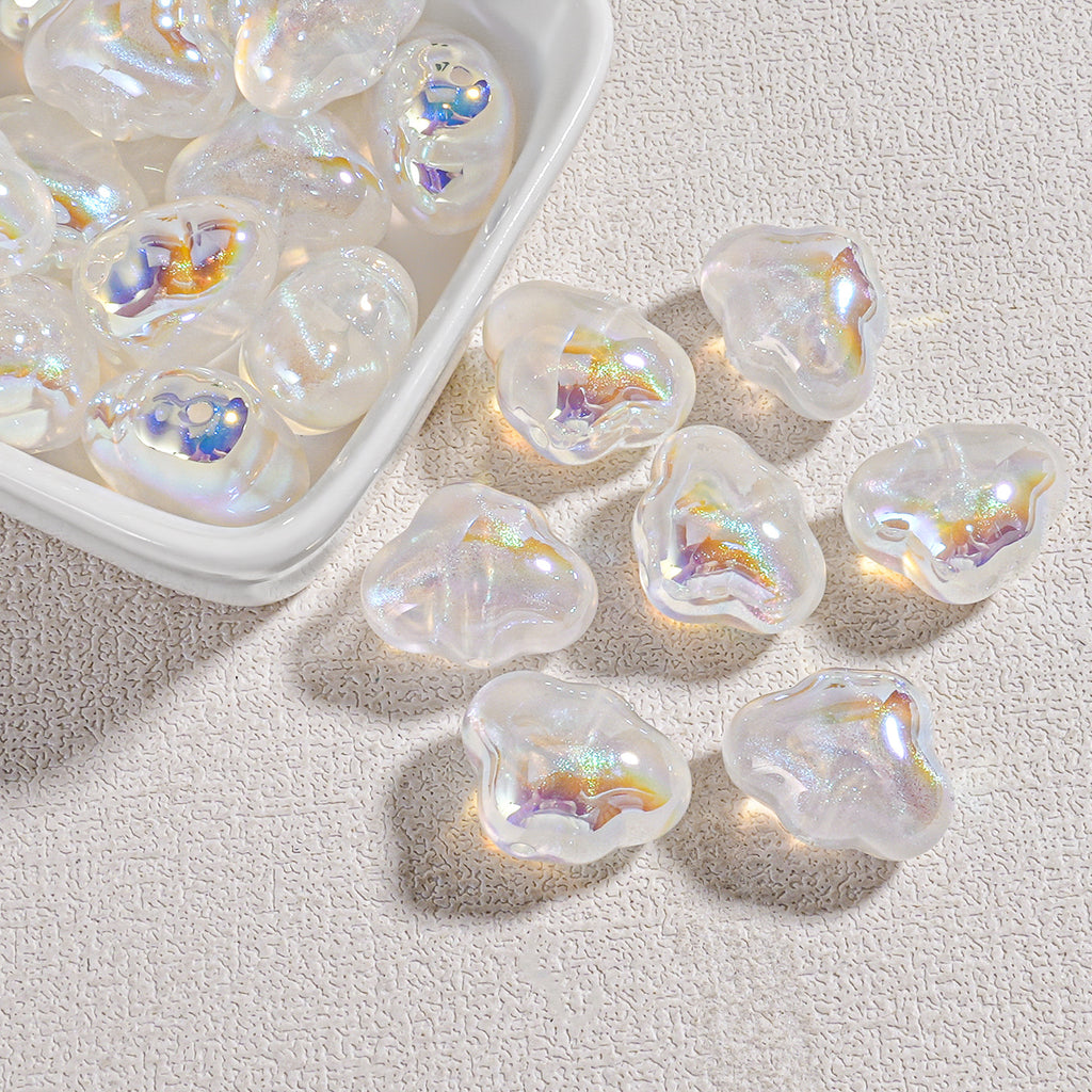 Clear cloud-shaped resin beads with iridescent oil-painting swirls in a white tray and on beige fabric