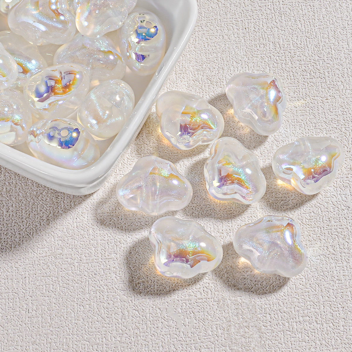 Clear cloud-shaped resin beads with iridescent oil-painting swirls in a white tray and on beige fabric