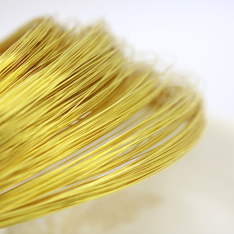 A close-up of a bundle of fine metallic gold wire strands, showing their texture and sheen against a soft white background.