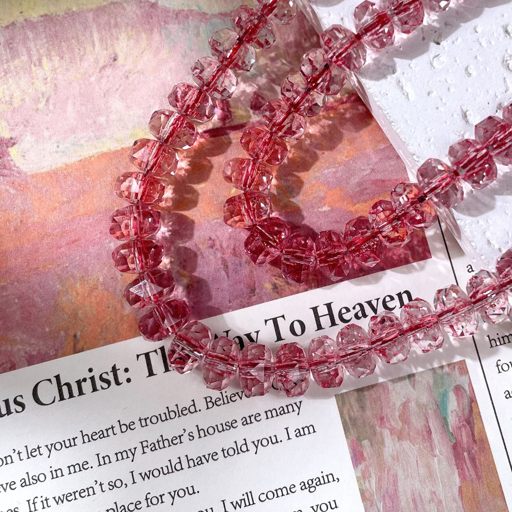 Strands of faceted pink crystal beads on a printed book page with a watercolor painting