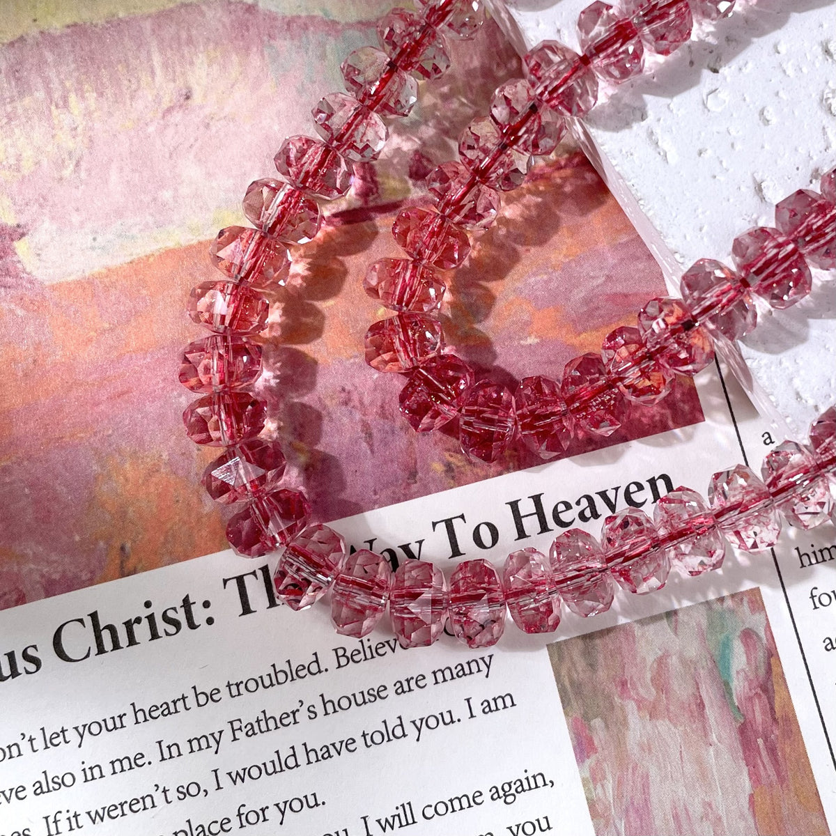 Strands of faceted pink crystal beads on a printed book page with a watercolor painting