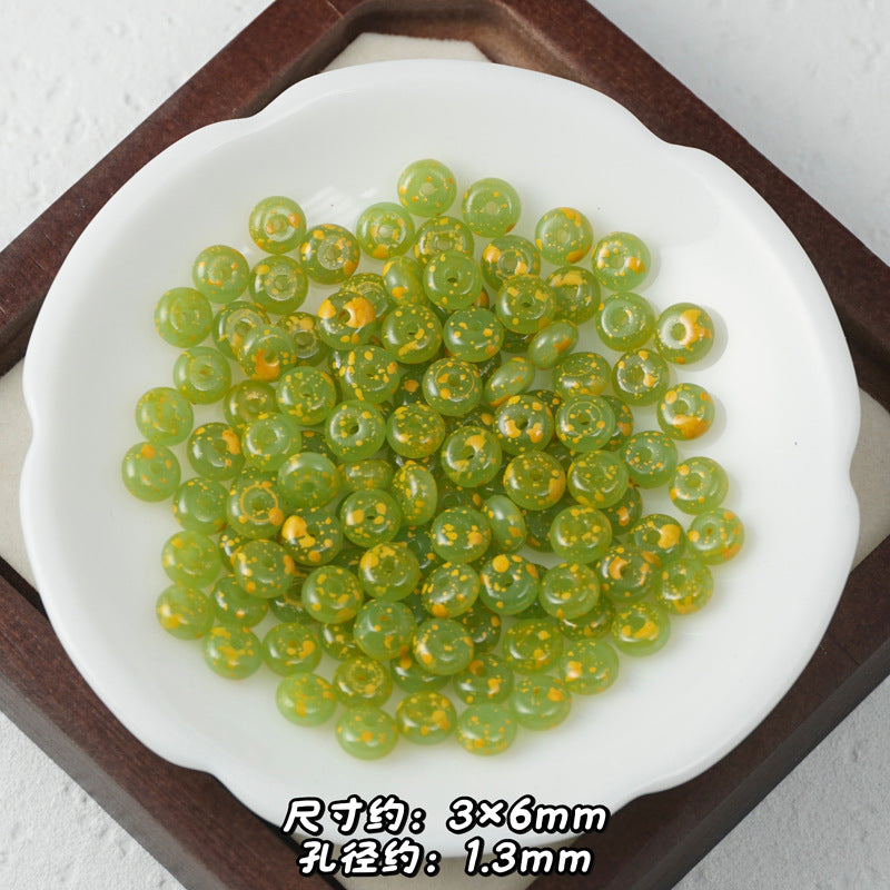 Green translucent Picasso glass abacus beads with gold glitter accents in a white scalloped dish.