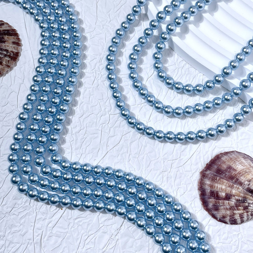 Light blue glass pearl bead strands in S-curves on white textured surface with seashells