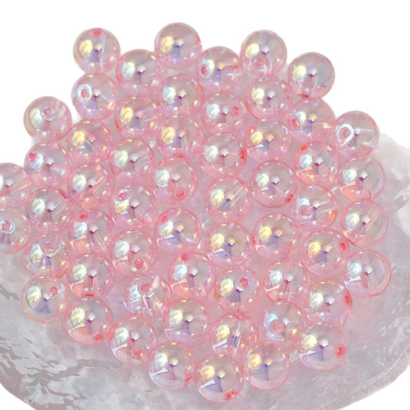A pile of round, transparent pink glass beads with an iridescent finish, arranged on a white textured surface against a white background.