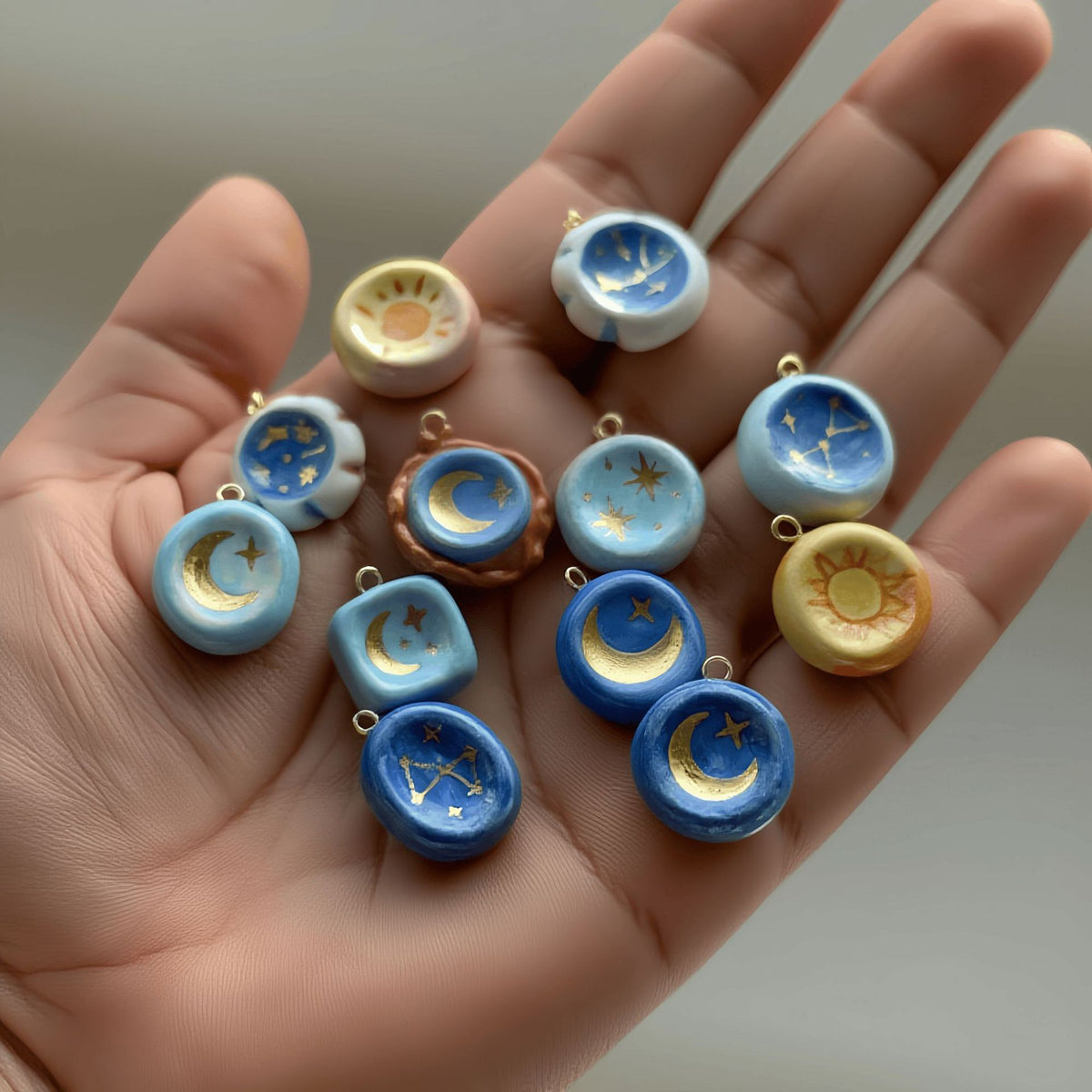 Hand holding various small ceramic or porcelain celestial-themed pendants.