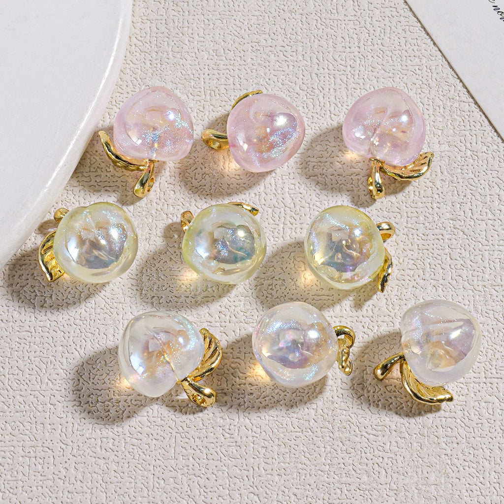Nine iridescent mini peach beads with gold leaf-shaped settings on a textured beige surface