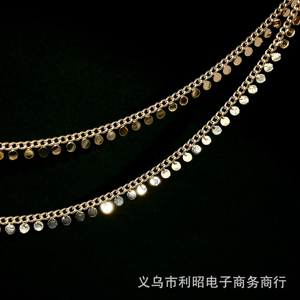 Two strands of gold-toned disc chain with small round metallic discs on a black background.