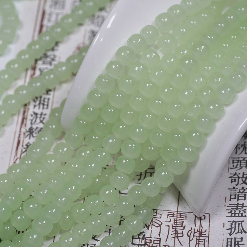 Light green faceted glass beads draped over a white ceramic spoon on top of printed paper.