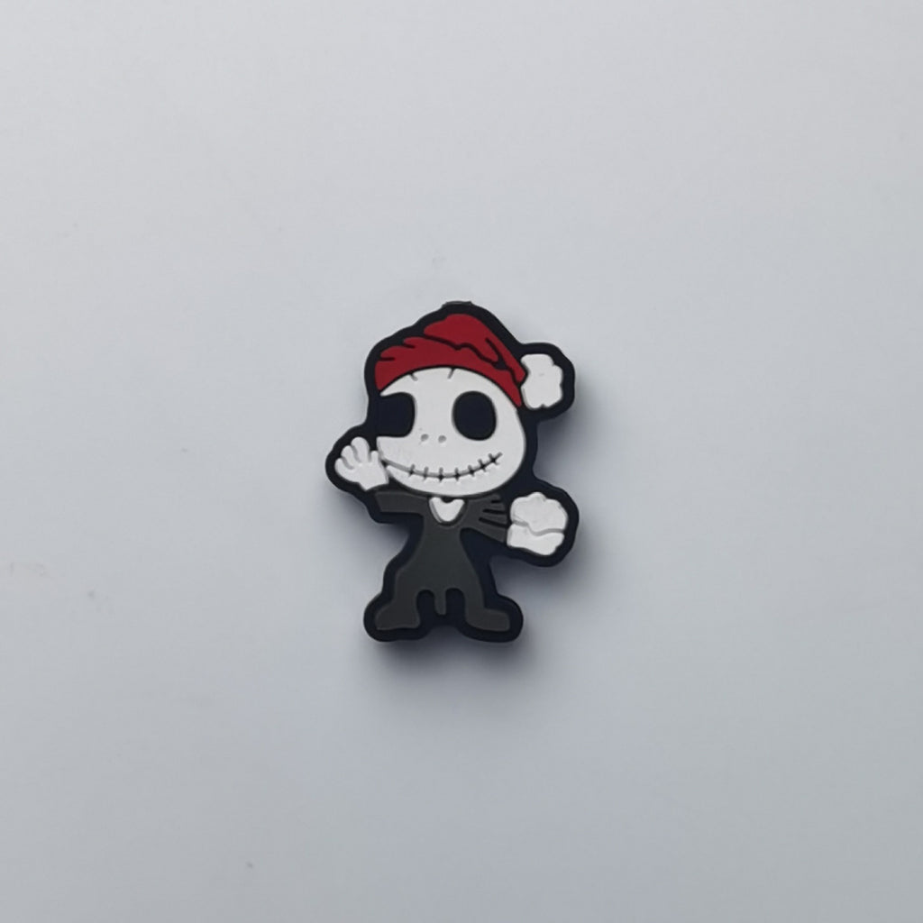 A small cartoon character charm or pin featuring a black and white skeleton figure wearing a red Santa hat, centered on a plain light gray background.