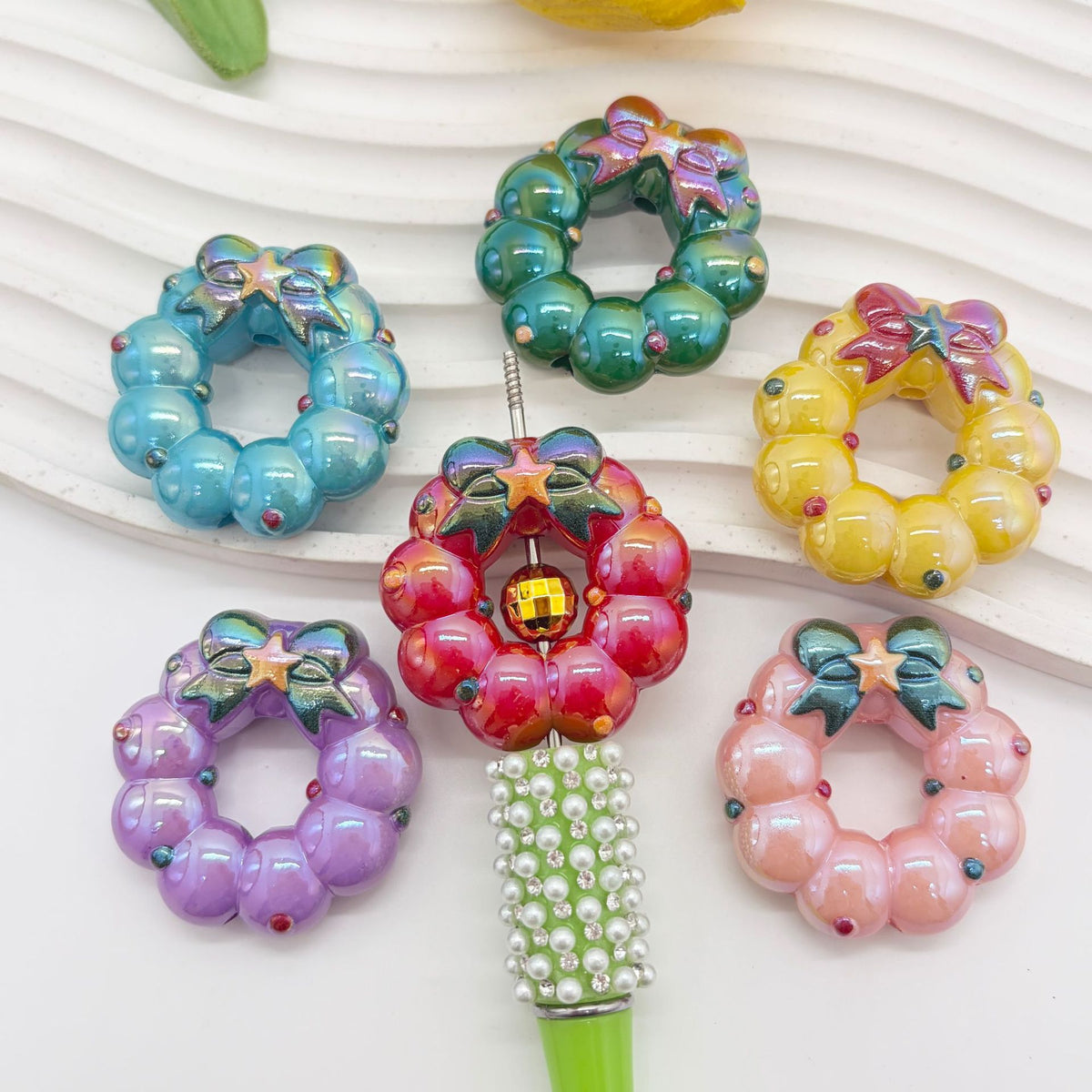 Six colorful wreath-shaped acrylic focal beads with bows and stars in blue, green, yellow, red, purple and pink