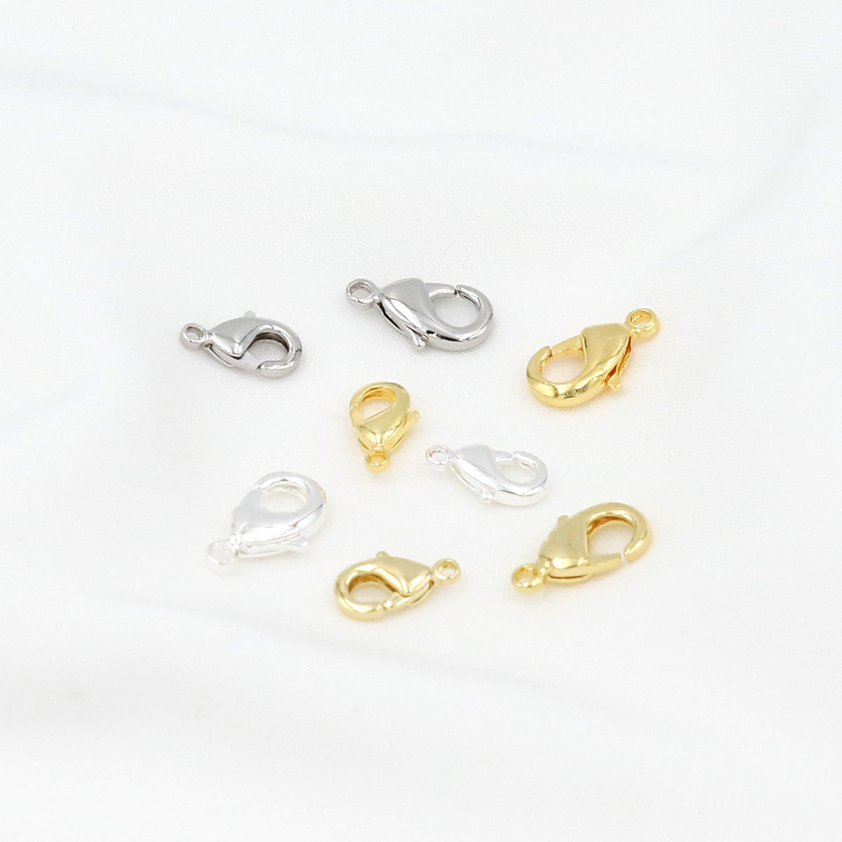 Eight gold and silver teardrop lobster clasps arranged on a white background