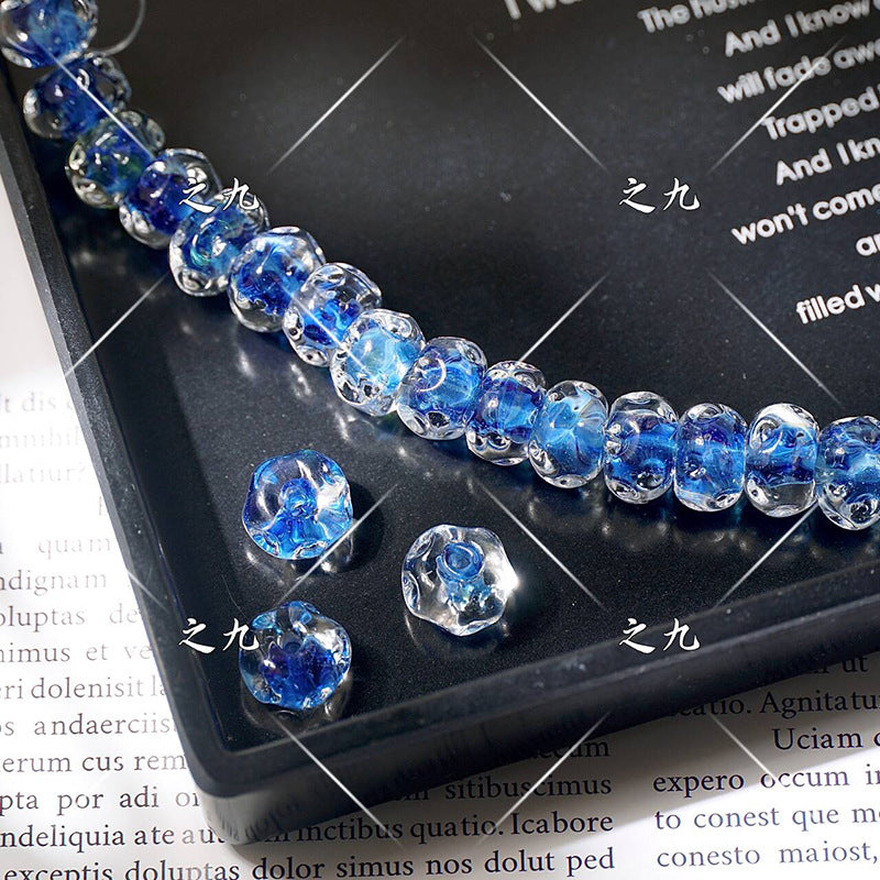 Strand of blue water-ripple lampwork glass beads on a black tray with three loose beads, over printed book text