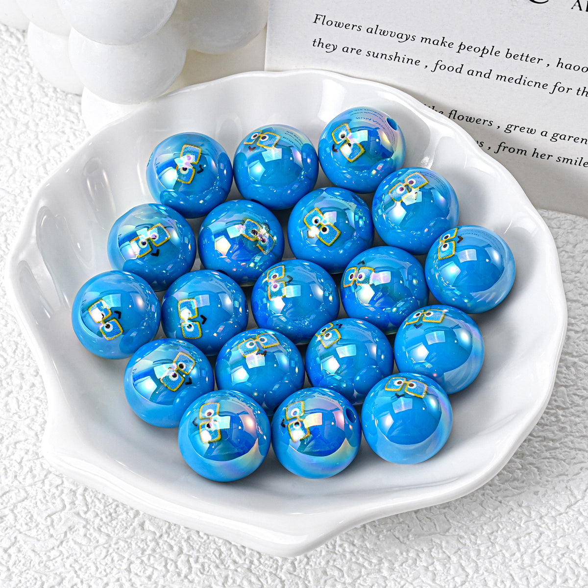 Glossy blue iridescent resin beads with cartoon owl prints in white ceramic dish on textured white surface