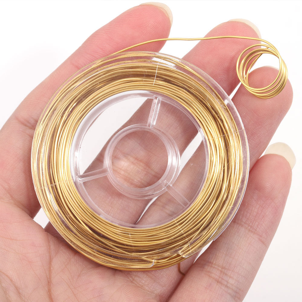 A hand holding a clear plastic spool wound with fine metallic gold wire, white background.