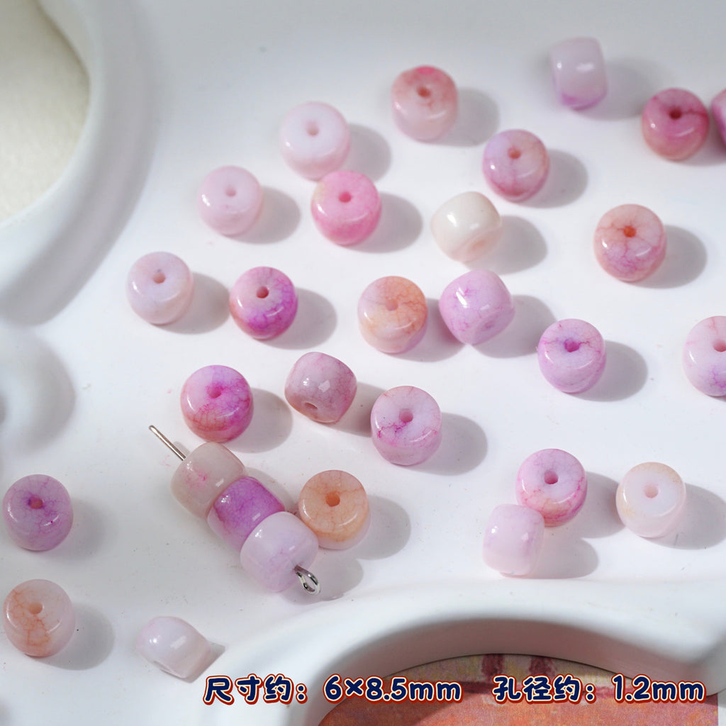 Pink and purple marbled round porcelain beads on white tray, one threaded