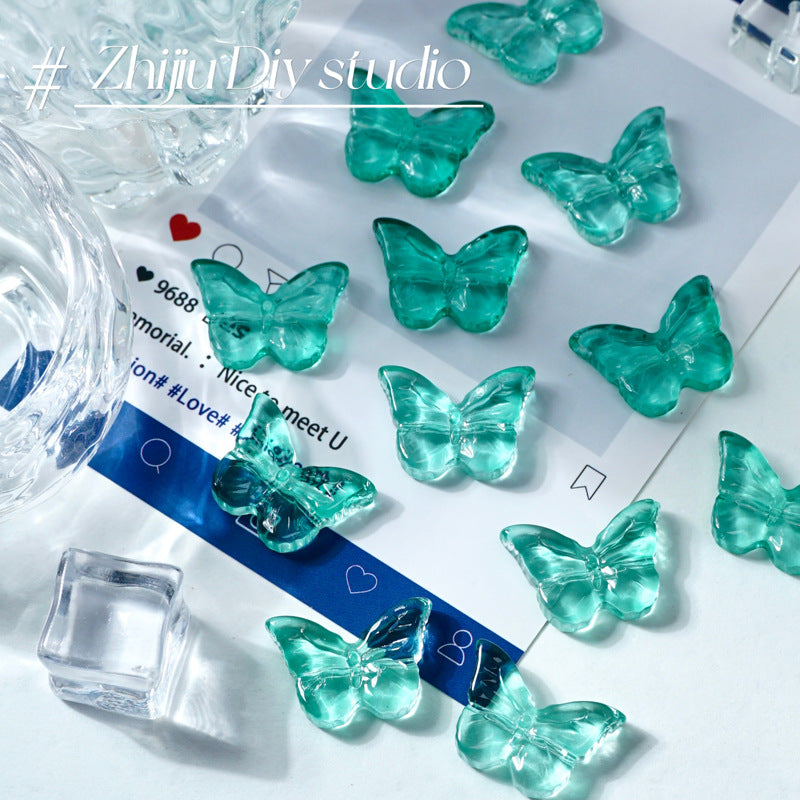 Translucent teal butterfly-shaped glass beads arranged on a glossy white surface