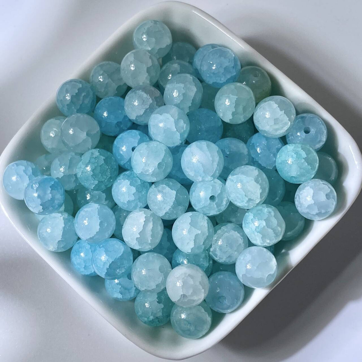 Light blue 10mm water-dyed jade-style crackle glass beads in a white square dish