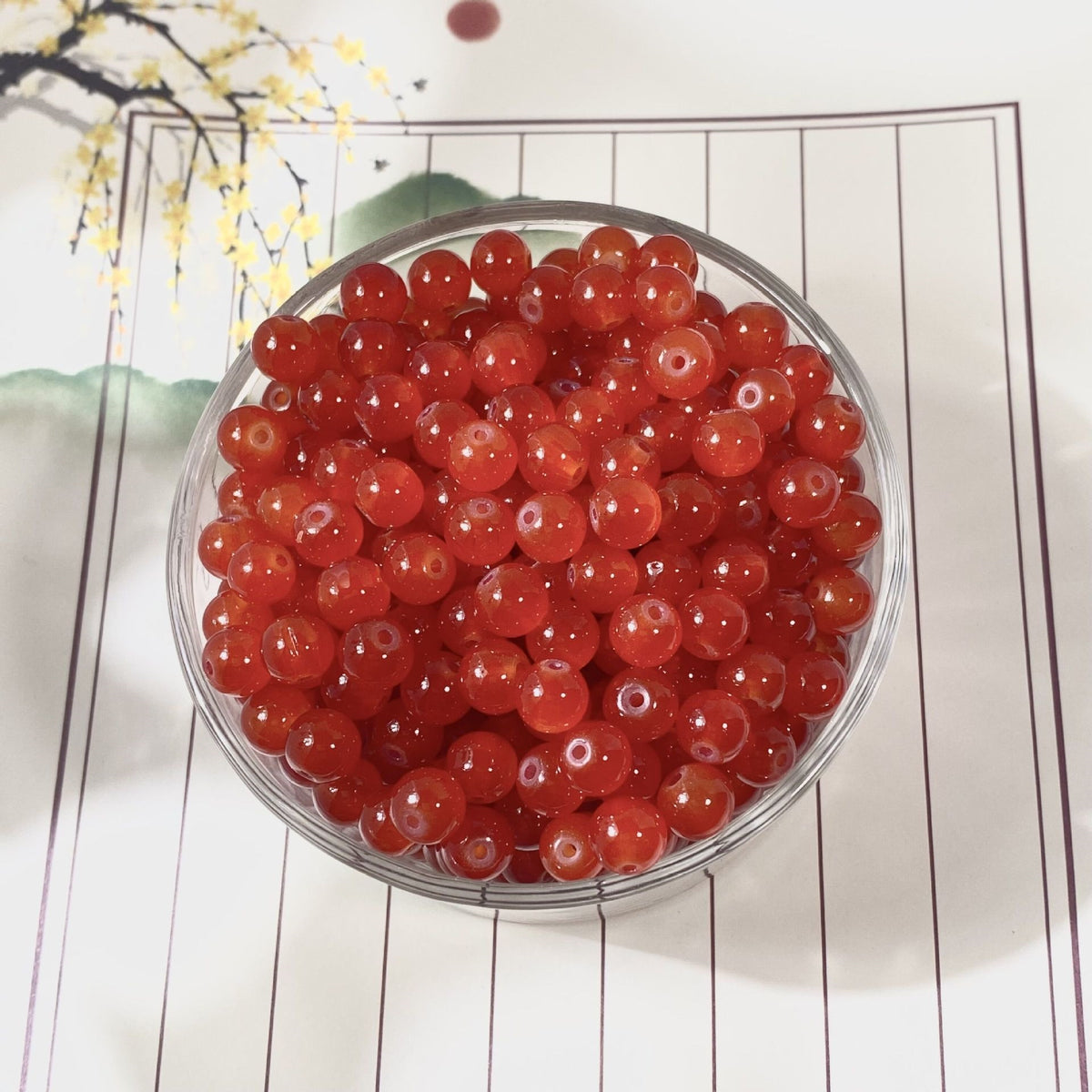 Glossy red translucent round beads in a clear glass bowl on decorative mat