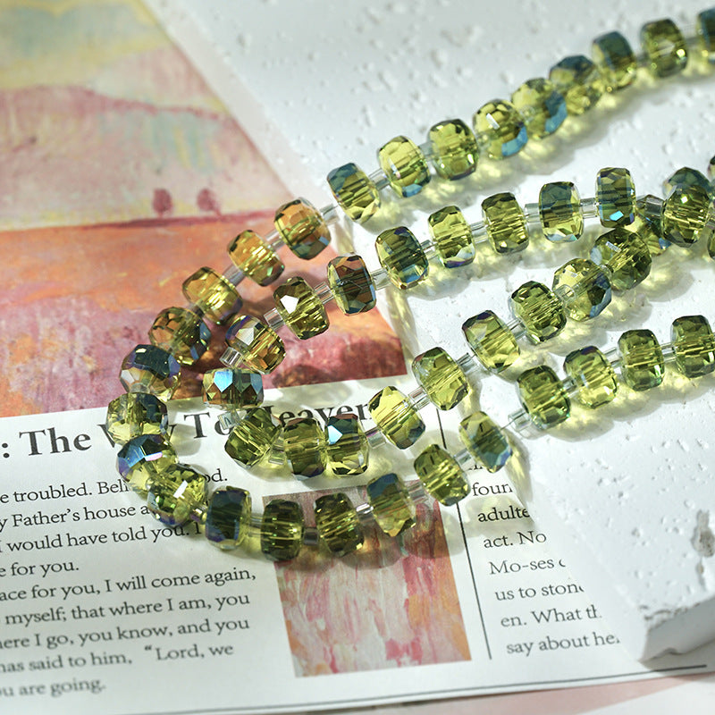 Close-up of faceted olive-green glass beads strung on clear cords arranged diagonally over an open book with printed text