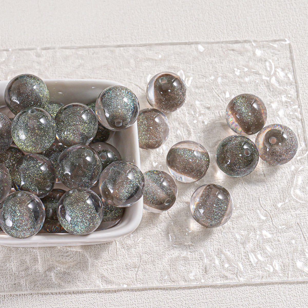 Iridescent glitter round beads in a white dish and scattered on textured white surface