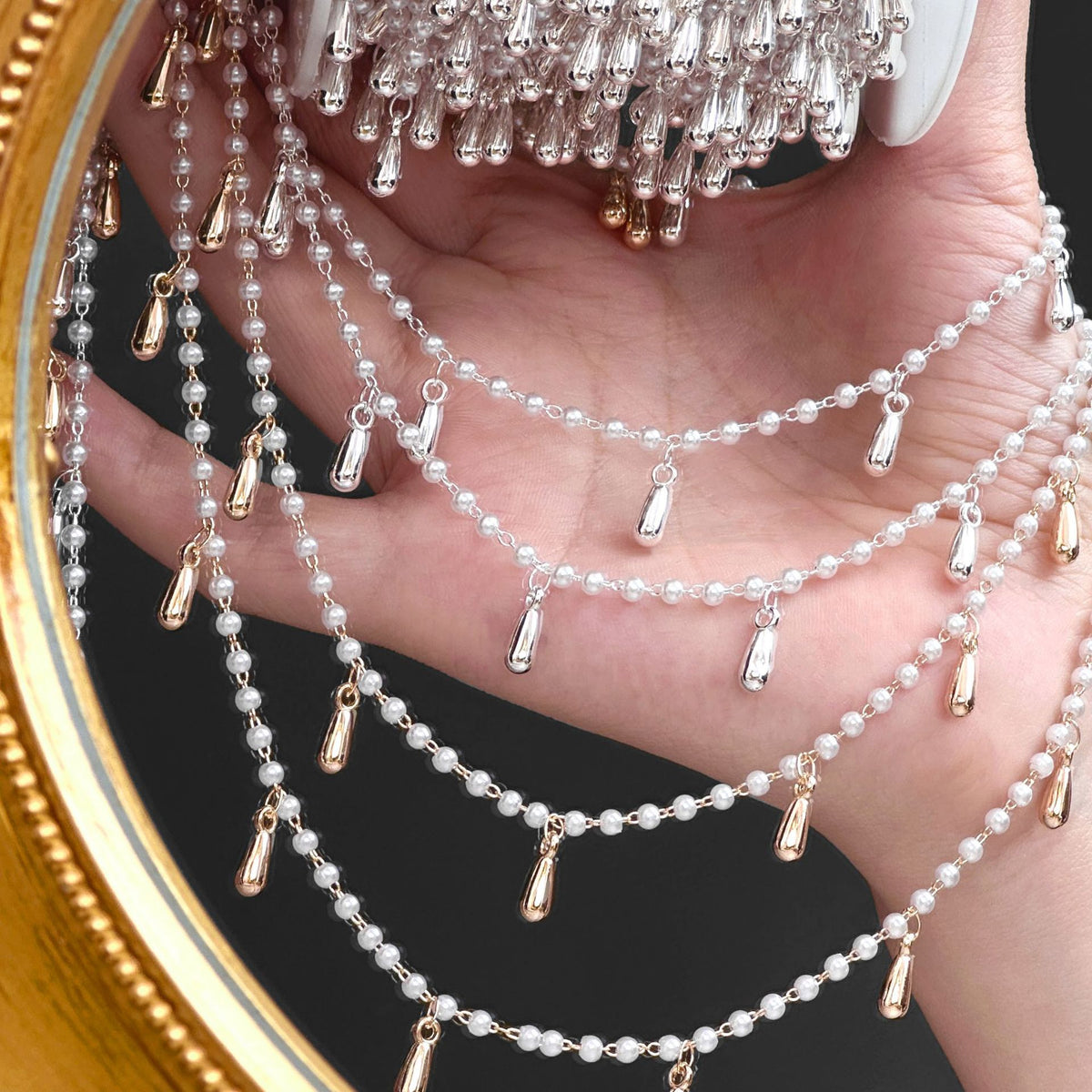 Hand holding layered faux pearl chains with silver and rose gold teardrop fringe charms