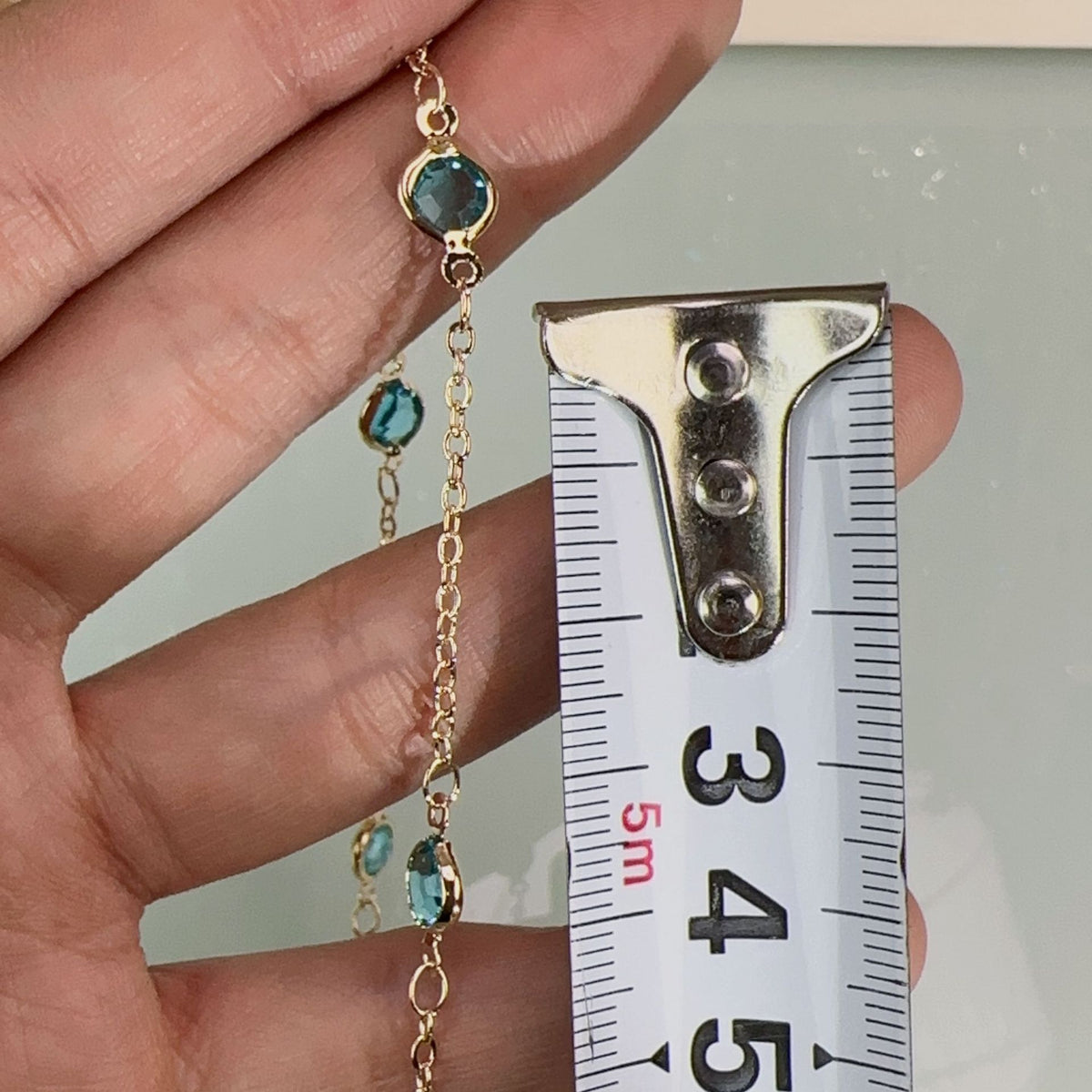 Gold chain bracelet with small teal-blue gemstone accents held in hand