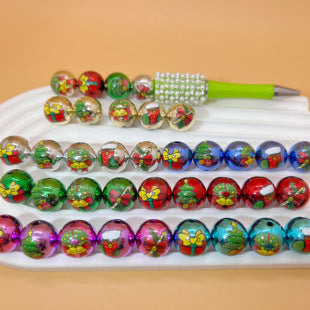 Colorful Christmas printed acrylic round beads in four rows on a white tray with a beaded pen on top