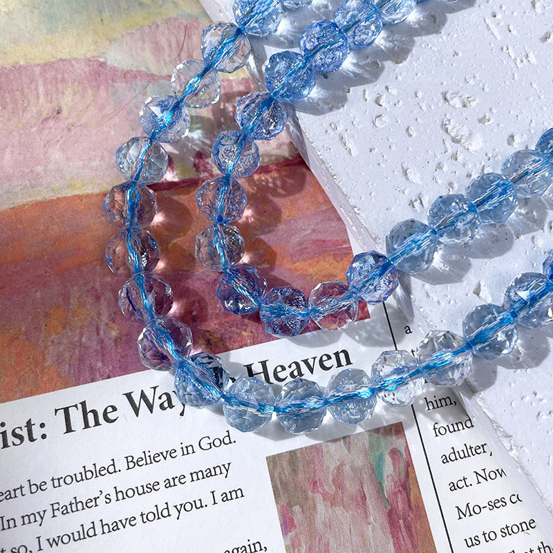 Strand of clear faceted glass beads with embedded light blue threads draped diagonally across a textured white surface