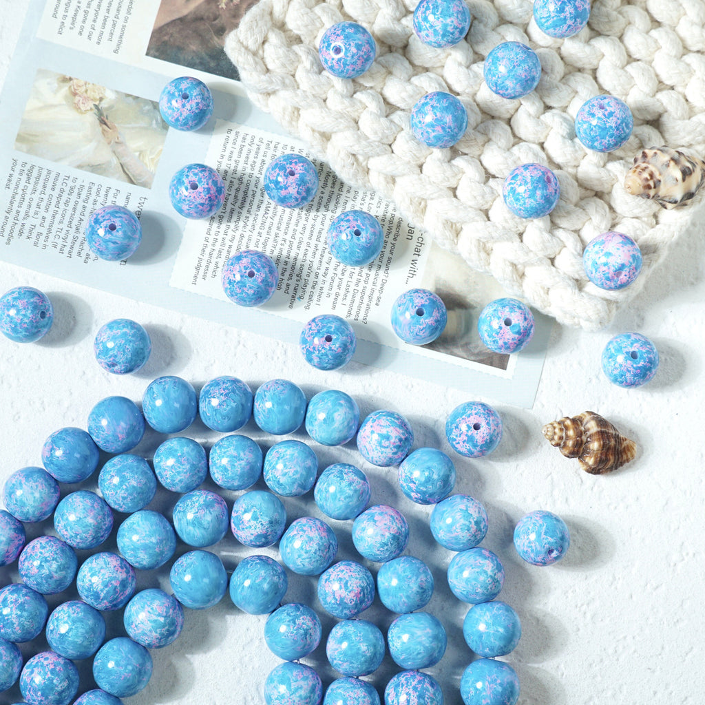 Blue marbled round glass beads with white and purple speckles on a white surface