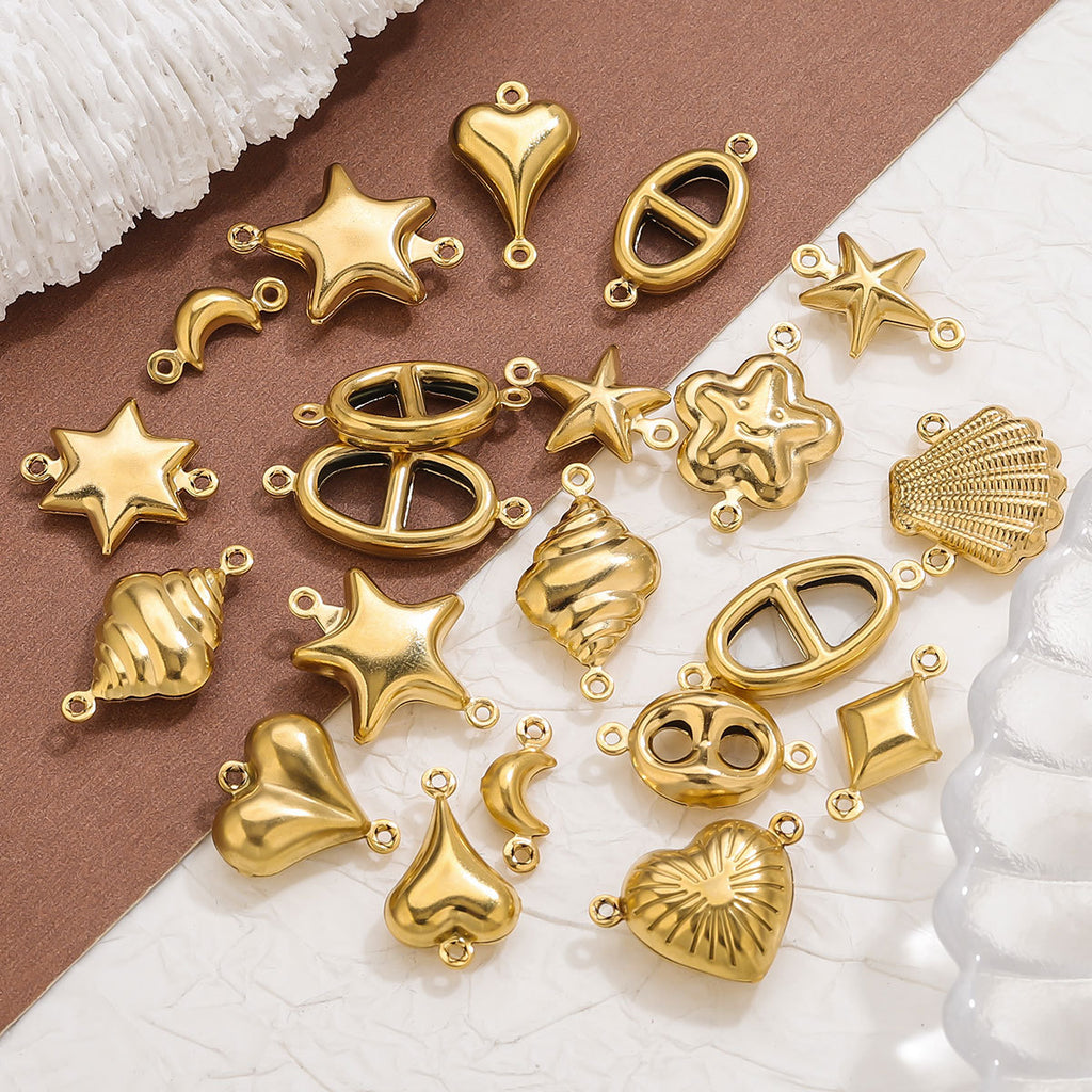 Gold-plated stainless steel double-hole hollow connector charms in heart, star, moon, and shell shapes on textured surface