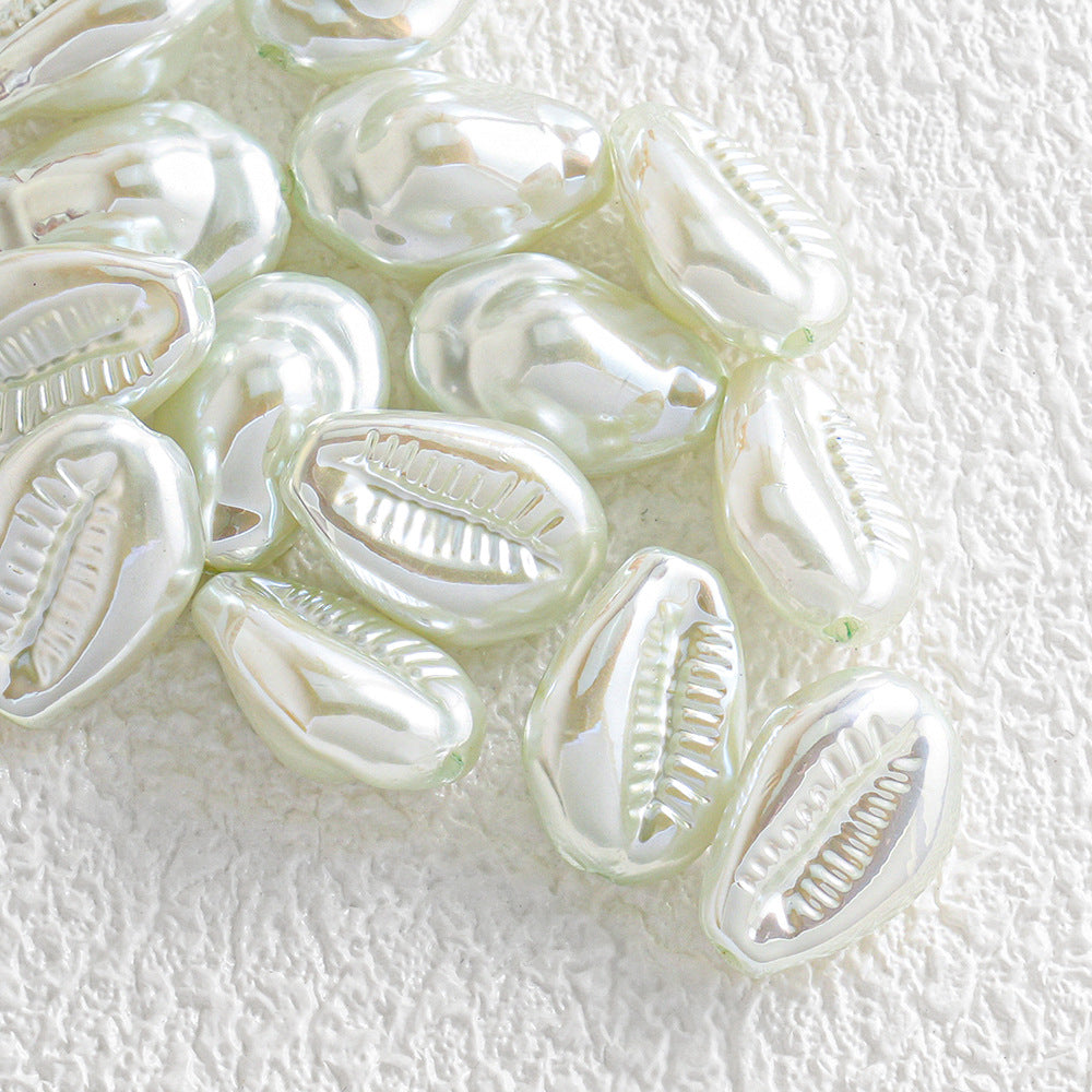 Group of glossy iridescent white cowrie shell-shaped beads on a textured white surface