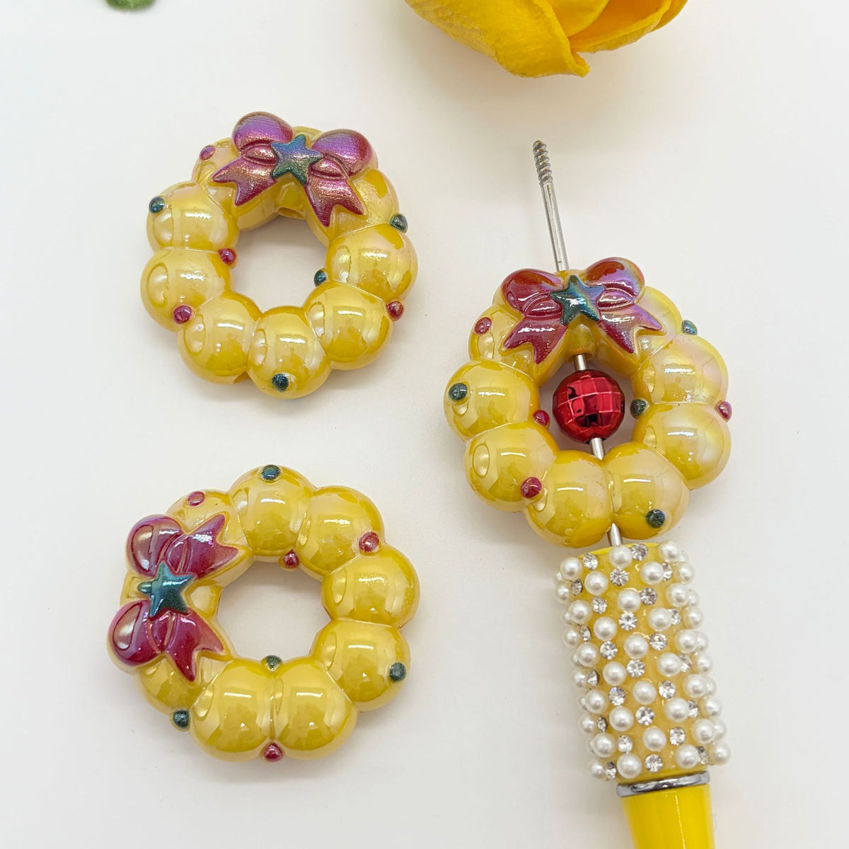 Three yellow wreath-shaped acrylic focal beads with colorful bow details on a white background
