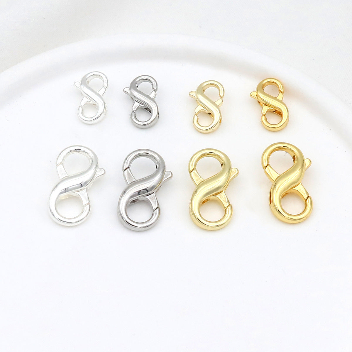 Eight figure-eight lobster clasps in two sizes and silver and gold finishes arranged in two rows on white