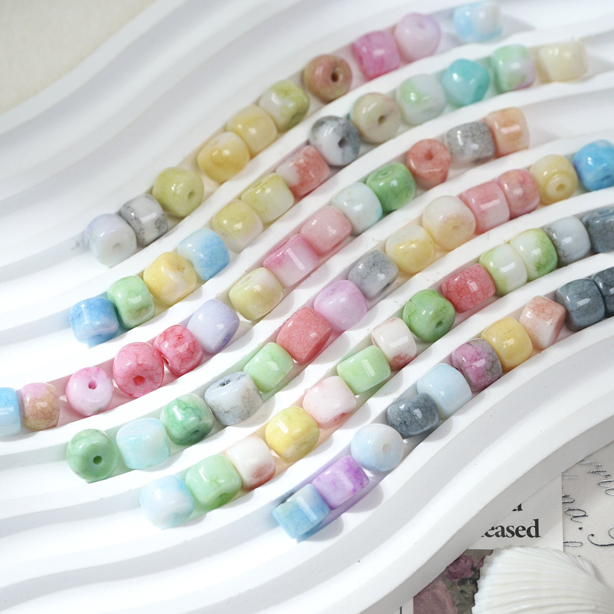 Multicolor cylindrical porcelain barrel beads with marbled pattern in diagonal rows on white