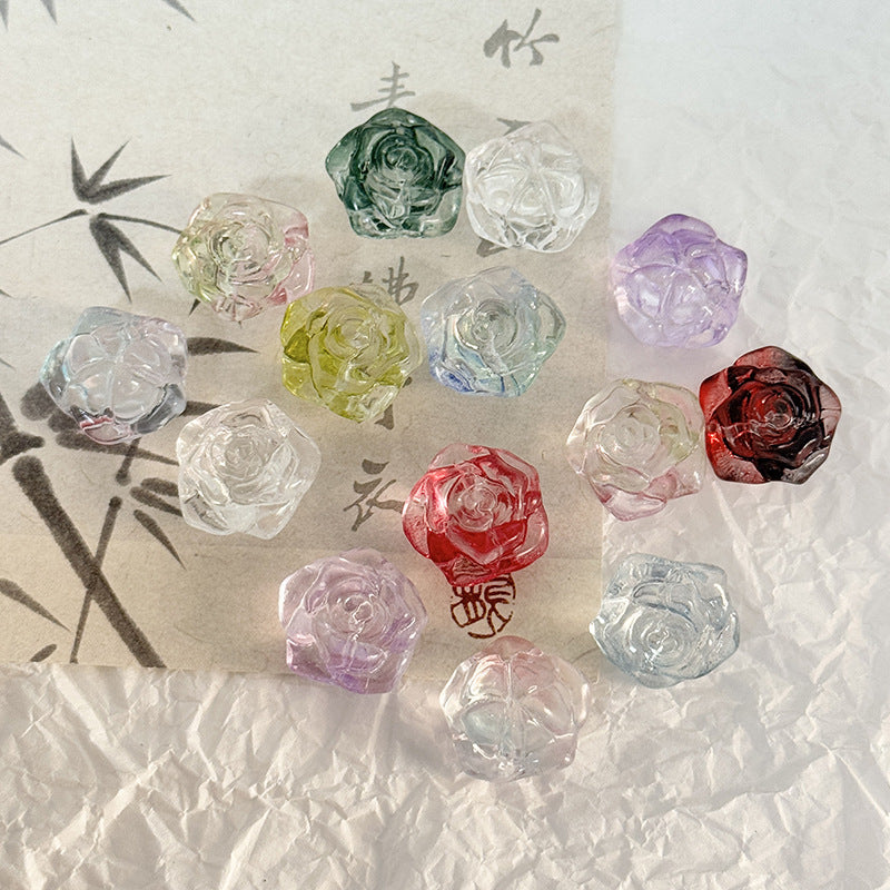 Translucent rose-shaped glass beads in green, purple, pink, red and clear on a textured white surface with decorative paper