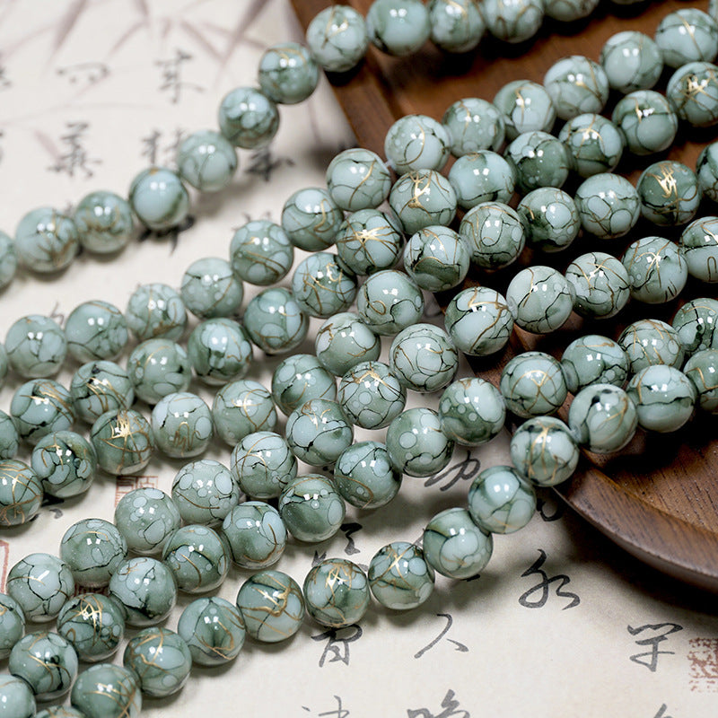 Close-up of pale green-gray marbled porcelain beads with gold veining on a light surface