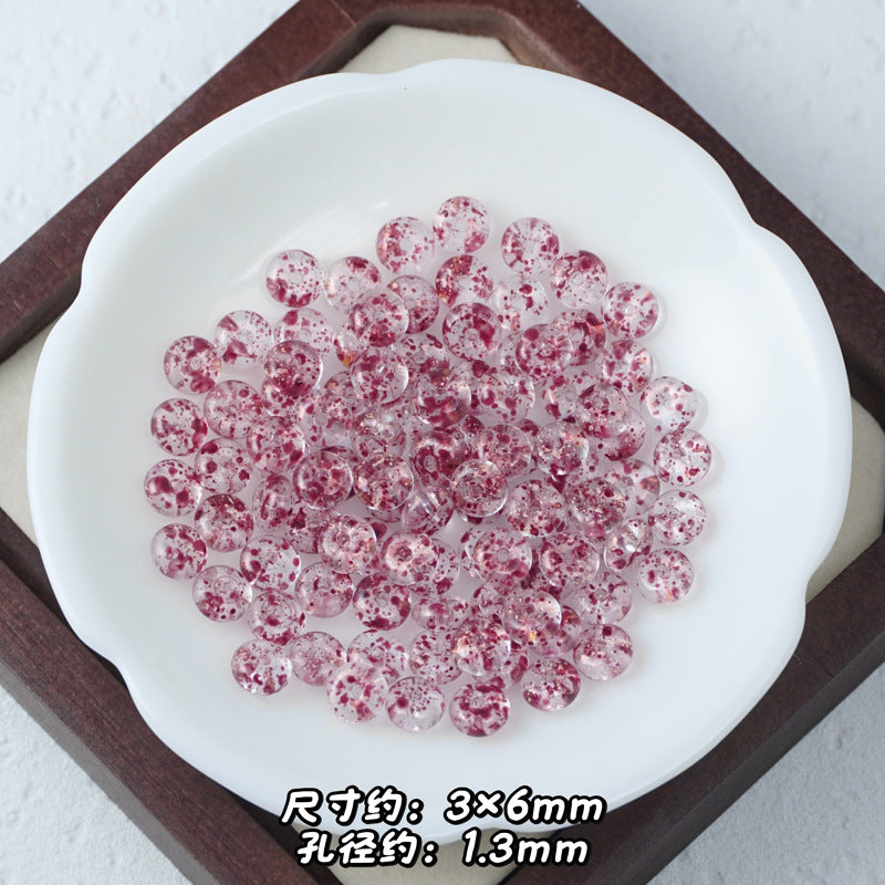 Clear Picasso glass abacus beads filled with pink and red glitter in a white scalloped dish.