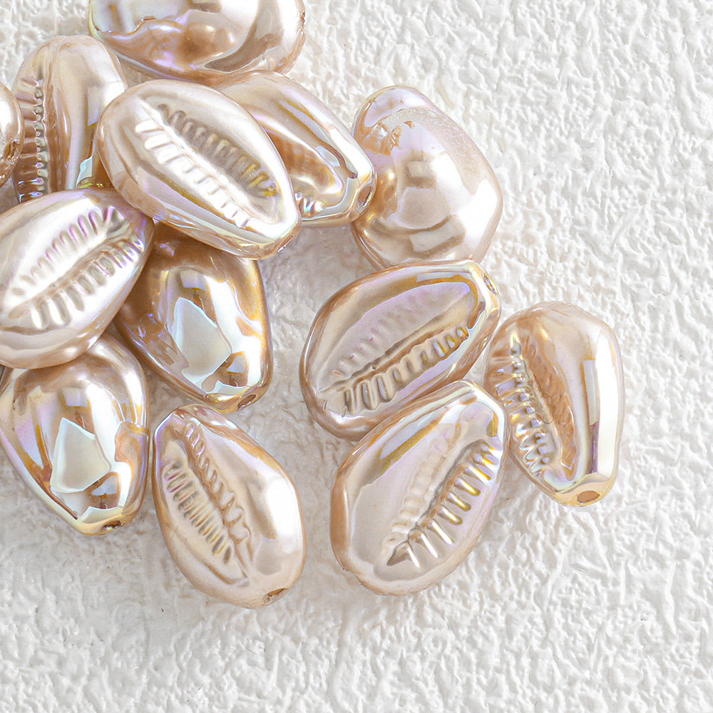 Pile of iridescent gold and rose gold cowrie shell beads on a textured white background